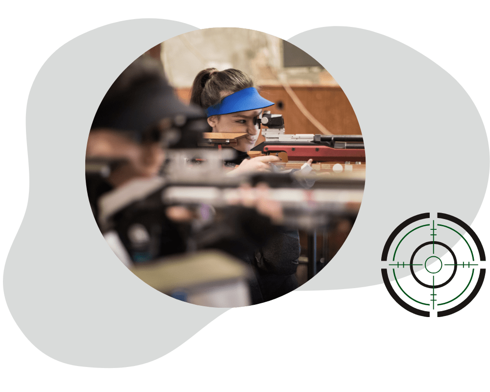 Frau mit Luftgewehr Frau zielt mit einem modernen Luftgewehr auf eine Schießscheibe in einer Schießhalle. Im Vordergrund ist ein stilisiertes Fadenkreuz-Logo zu sehen.